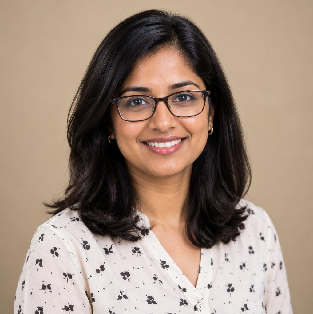 Studio portrait of a South Asian woman with glasses smiling in business casual attire